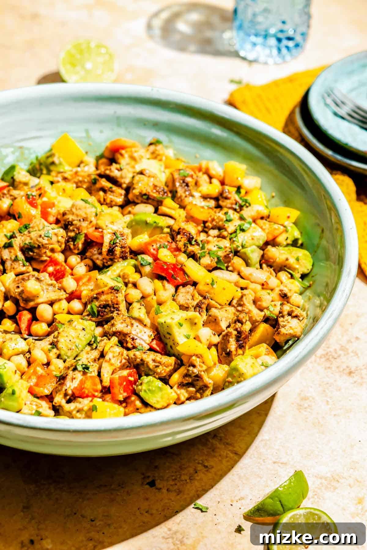 Chipotle Chicken Hearty Bean Salad 3 A close-up shot of the vibrant chipotle chicken dense bean salad served in a large blue bowl, with fresh lime wedges and blue serving plates arranged around it. The rich textures and colors of the ingredients are highlighted.