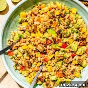 Chipotle chicken dense bean salad tossed in a large blue bowl with metal utensils, garnished with fresh lime wedges and accompanied by glasses of water.