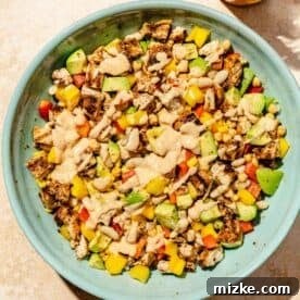 The vibrant chipotle chicken dense bean salad in a large blue bowl, now fully tossed with the creamy dressing drizzled generously on top, creating a glistening and well-mixed dish.