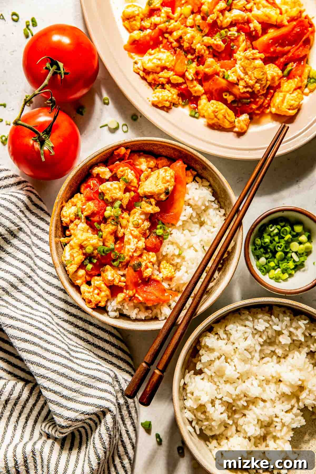 Savory Tomato Egg Scramble 4 An array of bowls filled with the vibrant Chinese tomato and egg stir fry, showcasing its rich colors and appetizing texture. Fresh, ripe tomatoes and a bowl of bright green chopped scallions are arranged nearby, along with elegant chopsticks, highlighting the freshness and traditional presentation of the meal.