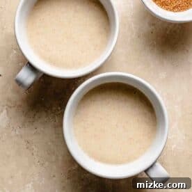 Snickerdoodle Mug Magic 9 Two white mugs filled with batter on a marble surface, accompanied by a small bowl of cinnamon sugar nearby.