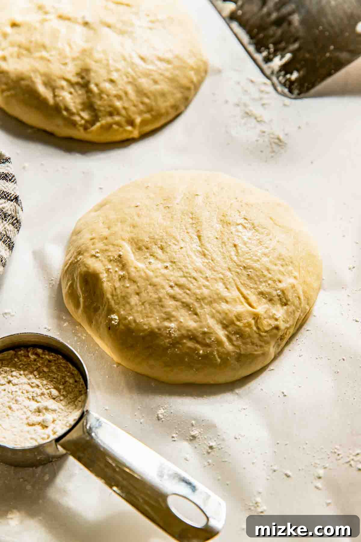 Crispy Thin Crust Pizza Dough Recipe 4 Various balls of raw, unbaked dough, perfectly portioned and ready for stretching, are arranged on a lightly floured wooden surface, with a metal measuring cup full of flour nearby, highlighting the preparation stage for thin crust pizza.