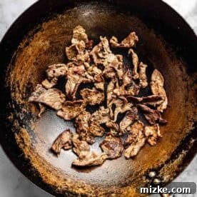 Cooked beef strips in a wok on a marbled surface.