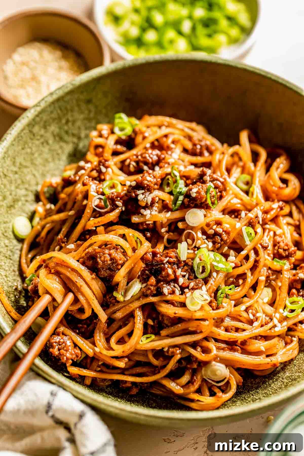 Sticky Mongolian Beef Noodles 4 A bowl of Mongolian ground beef noodles, generously sprinkled with fresh green onions and white sesame seeds. Chopsticks are placed alongside the bowl, inviting a taste.