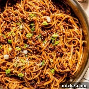 A pan of stir-fried noodles with minced meat, topped with sliced green onions and sesame seeds.