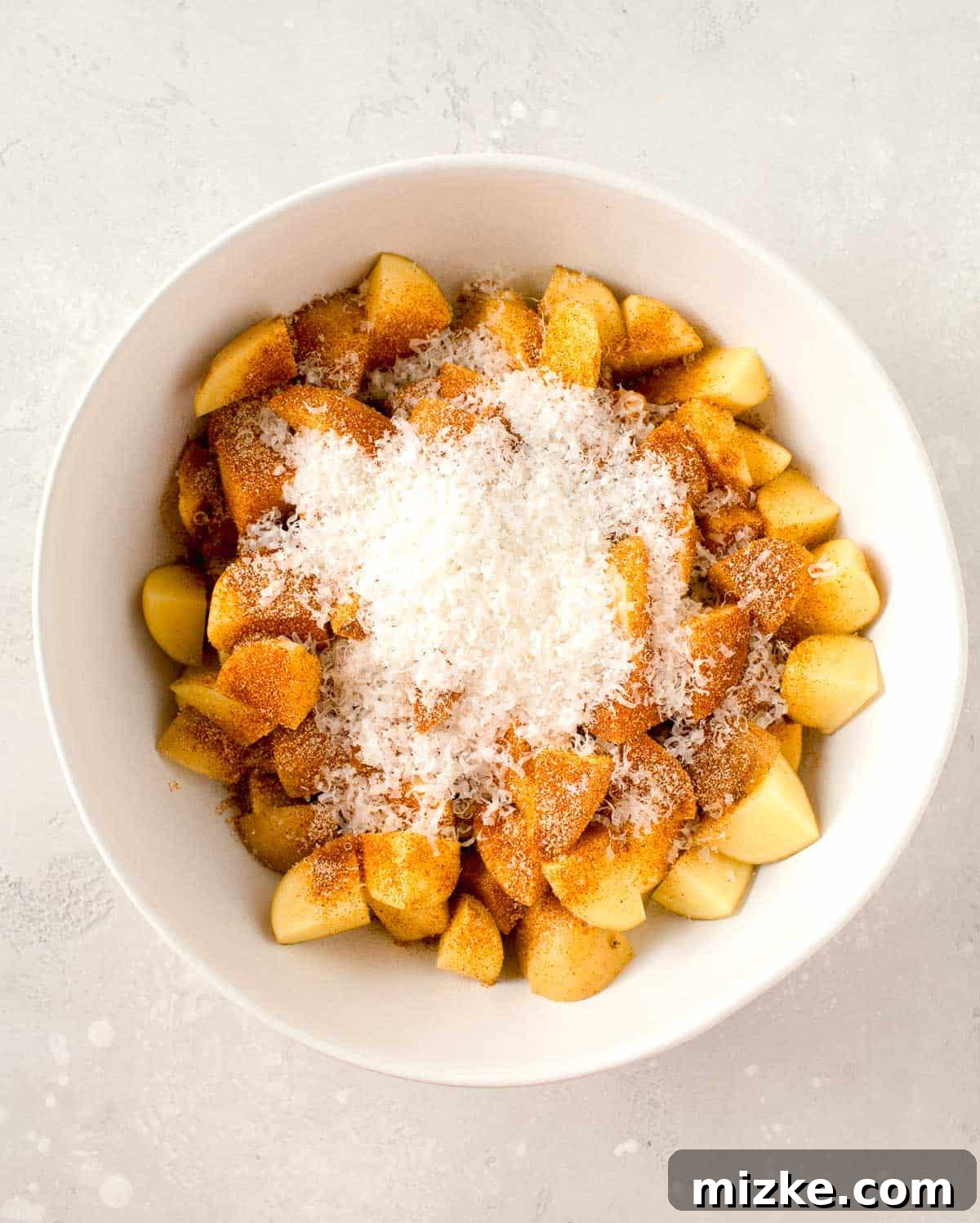 Crispy Garlic Parmesan Potatoes 4 seasonings and freshly grated parmesan cheese on top of potatoes in a white bowl