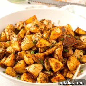 roasted parmesan potatoes in a large white bowl with gold metal spoon