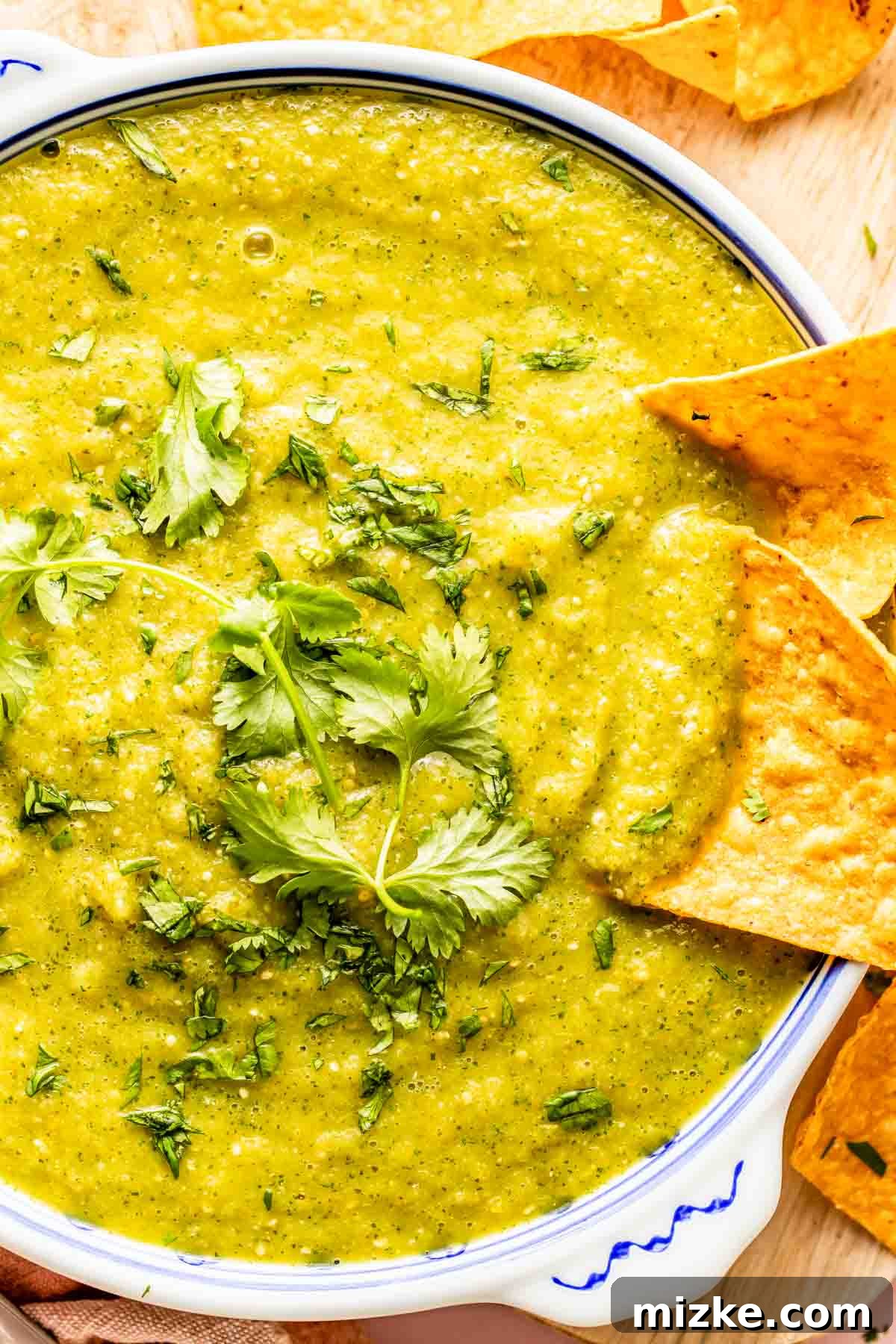 Fire-Roasted Salsa Verde 3 A bowl of green salsa garnished with fresh cilantro, surrounded by tortilla chips.