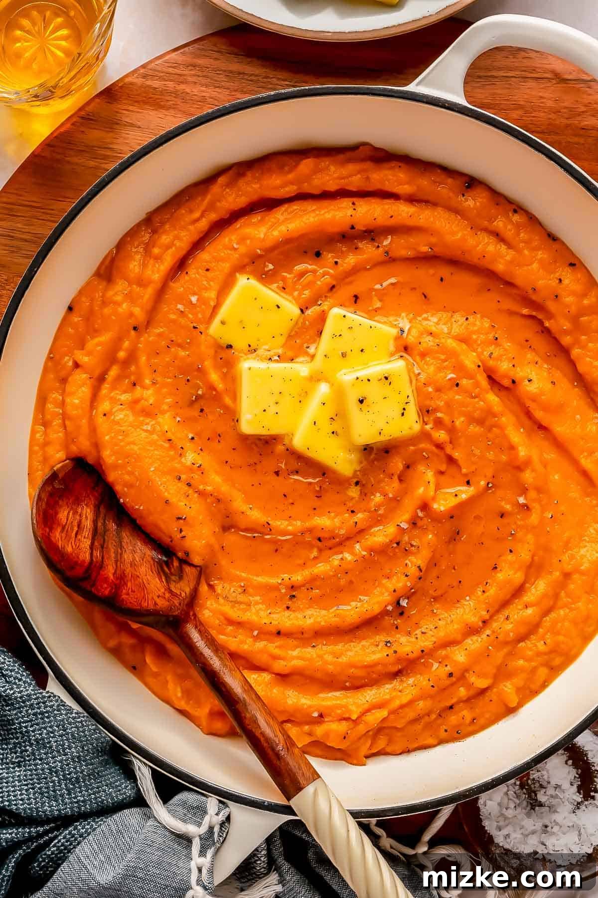 Whipped Sweet Potatoes 2 mashed sweet potatoes in a white dutch oven with 5 pads of butter on top with a wooden spoon in the center