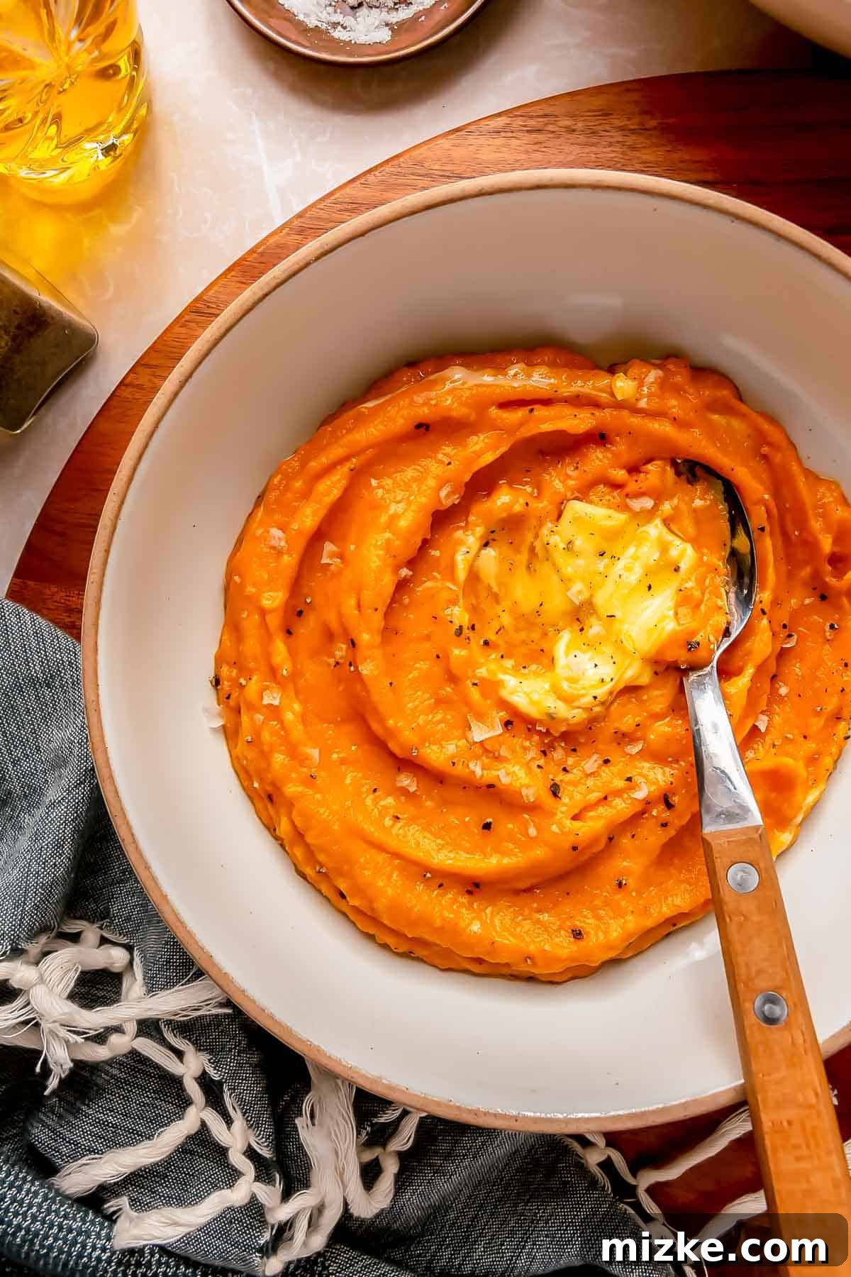 Whipped Sweet Potatoes 4 mashed sweet potatoes in a white bowl with a spoon in the center. there are two pads of melted butter on top
