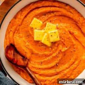 mashed sweet potatoes in a white dutch oven with 5 pads of butter on top with a wooden spoon in the center