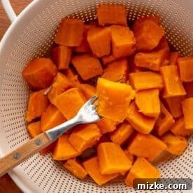 a fork pierces a cooked sweet potato in a white colander