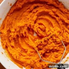 sweet potatoes are mashed in a white bowl with a potato masher