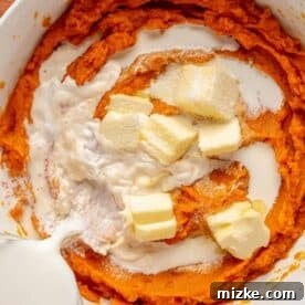pads of butter and milk is being poured on top of mashed sweet potatoes in a white bowl