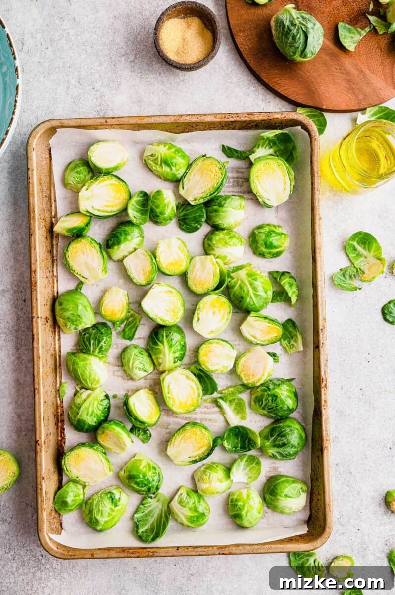 Crispy Garlic Roasted Brussels Sprouts 3 Raw Brussels sprouts, neatly sliced in half lengthwise, arranged on a baking sheet lined with parchment paper, ready for roasting.