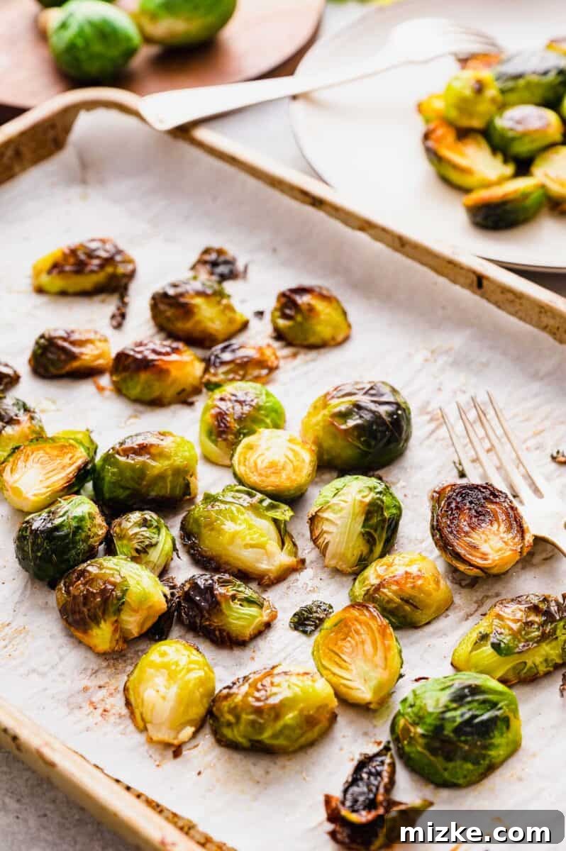 Crispy Garlic Roasted Brussels Sprouts 5 A large batch of freshly roasted Brussels sprouts scattered across a rimmed baking sheet, showcasing their varied textures and golden-brown hue.