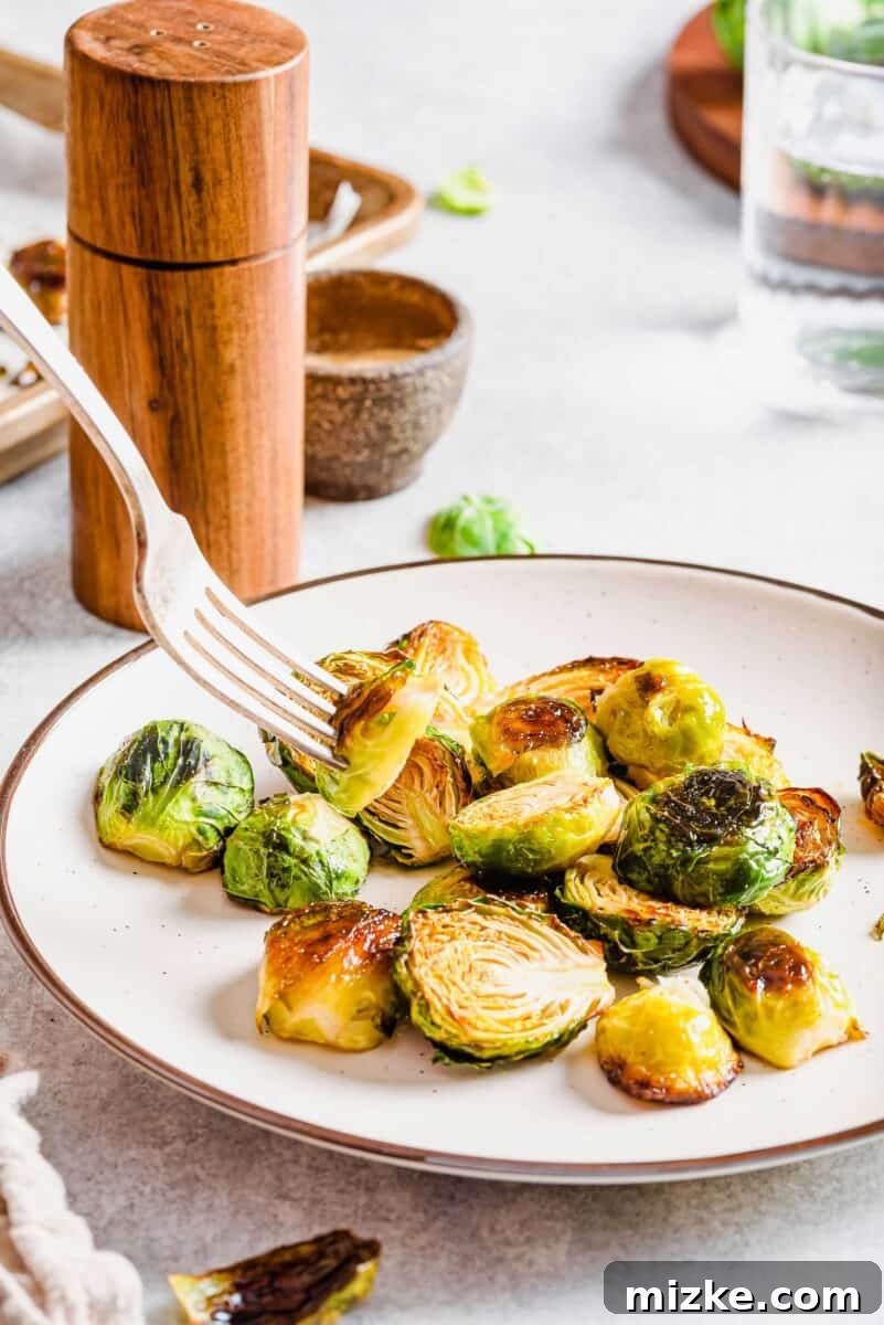 Crispy Garlic Roasted Brussels Sprouts 6 Roasted Brussels sprouts beautifully arranged on a white plate with a brown rim, with one sprout delicately held at the end of a fork, ready to be eaten.