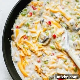 Vegetable mixture with milk and cream of mushroom and shredded cheese in a skillet with a wooden spoon.