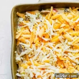 Freshly shredded cheese on top of spaghetti mixture in a casserole dish.