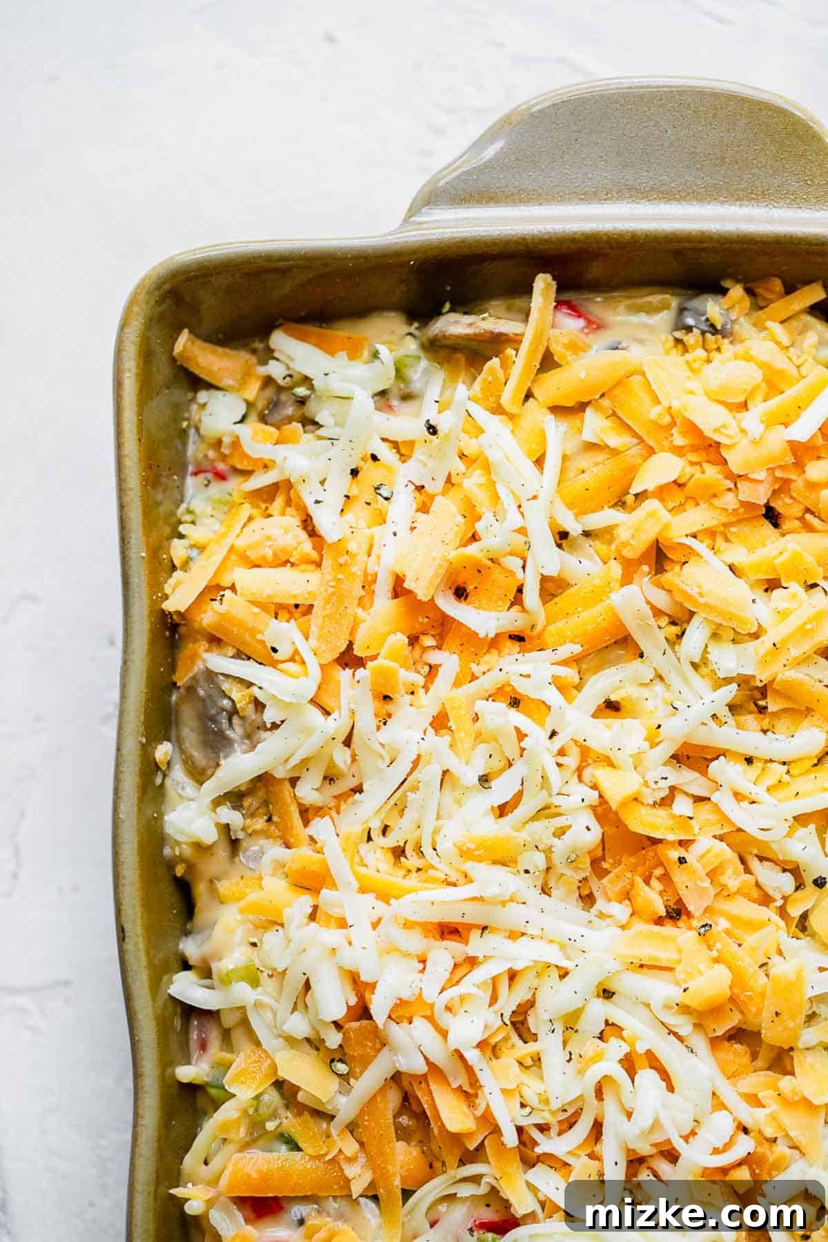 Cheesy Spaghetti Bake 6 Freshly shredded cheese generously spread on top of the spaghetti mixture in a casserole dish, ready for baking.