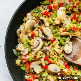 Mushrooms, celery, onions, and bell peppers in a large skillet with a wooden spoon.