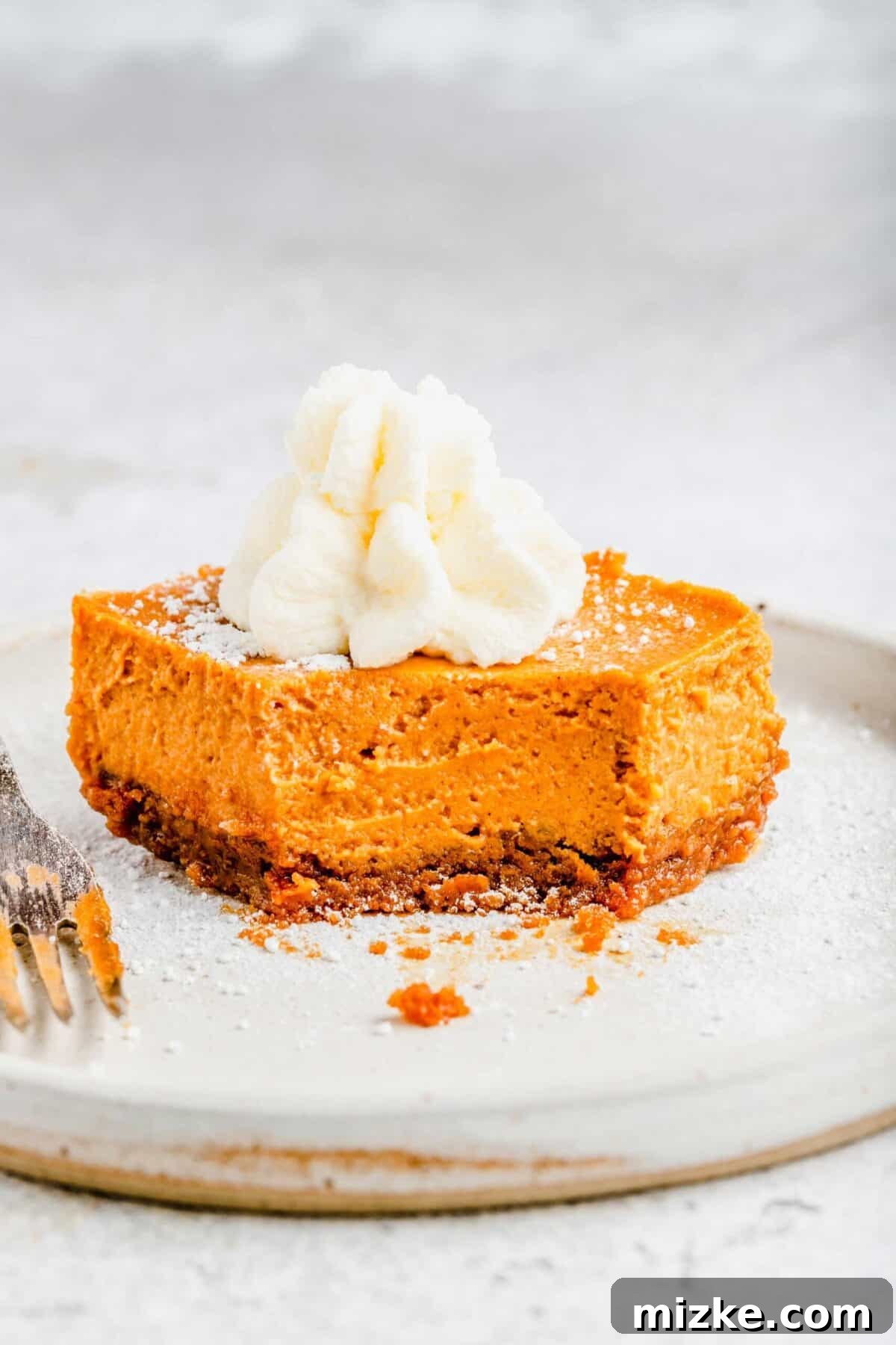 A delicious maple pumpkin cheesecake bar, enjoyed with a fork, topped with whipped cream, highlighting its inviting texture and rich fall flavors. A slice of maple pumpkin cheesecake bar on a plate, topped with whipped cream, with a bite taken out of it and a fork on the plate