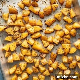 Cubed roasted potatoes on a metal baking sheet, seasoned and baked until golden brown.