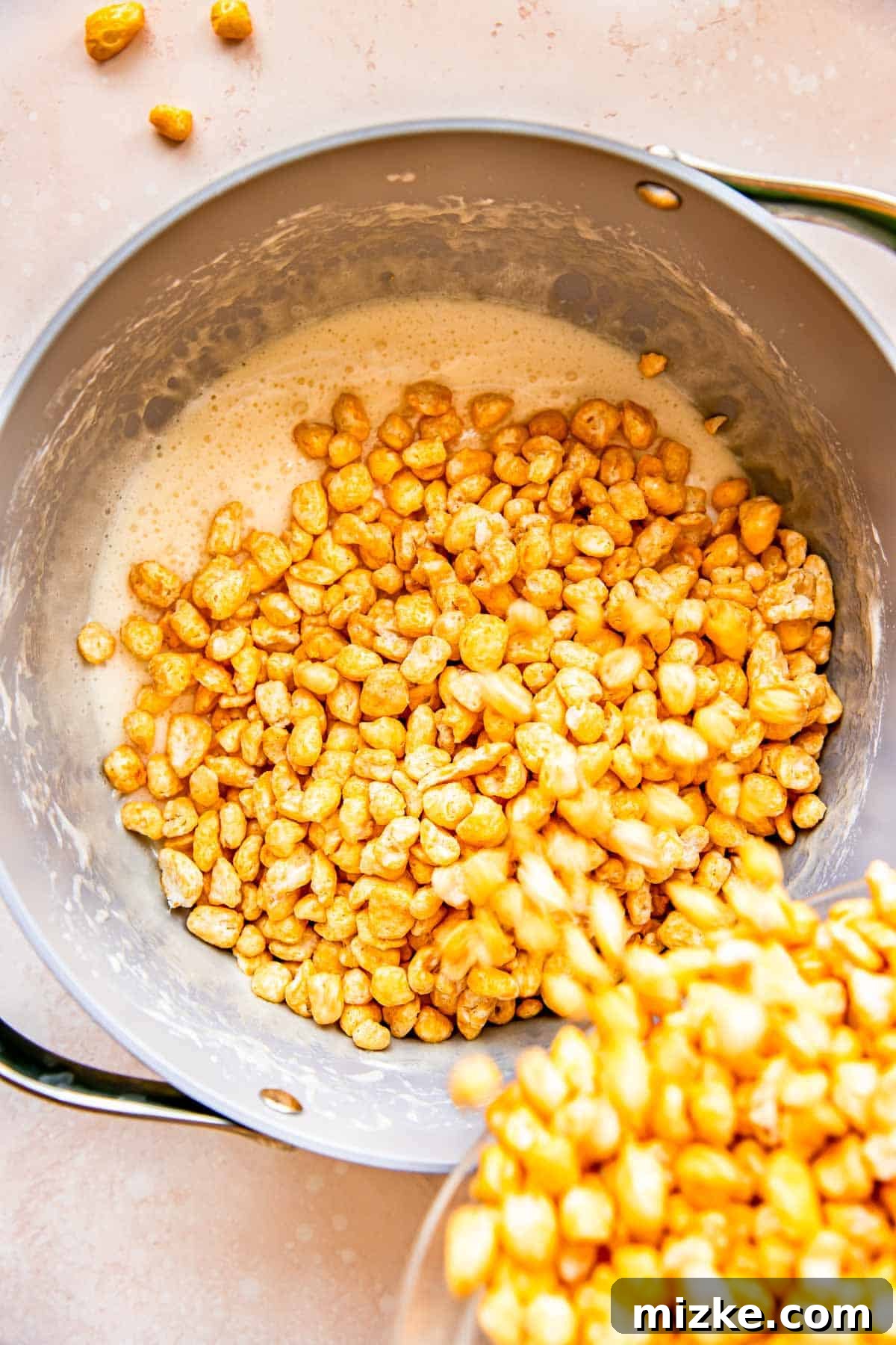 Wholesome Grain Bars 7 Corn Pops cereal is being poured into the pan, joining the melted marshmallow and butter mixture.