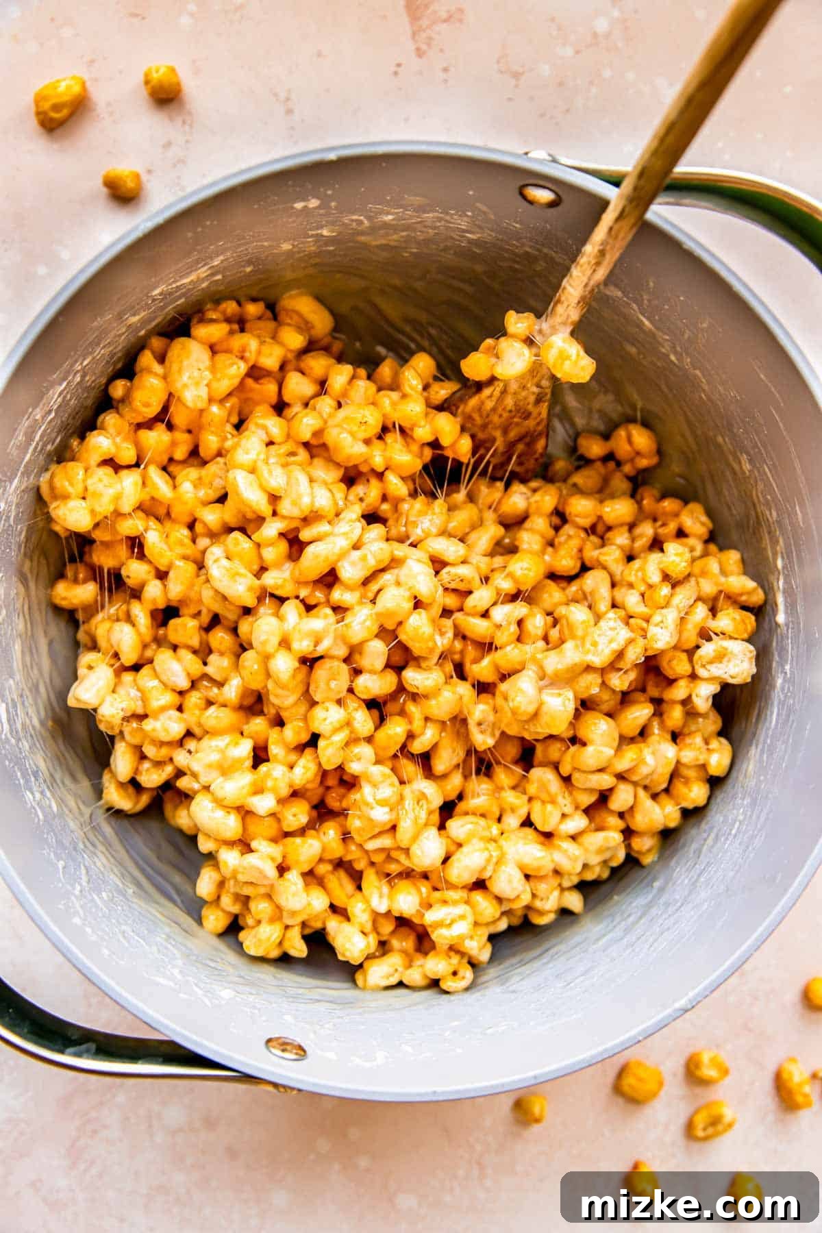 Wholesome Grain Bars 8 A wooden spoon is actively stirring the Corn Pops cereal into the marshmallow mixture, ensuring full coating.