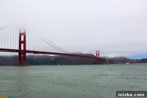 The Golden Gate Bridge stands majestically, a symbol of San Francisco. A wide-angle view of the Golden Gate Bridge, partially shrouded in fog, from Crissy Field.