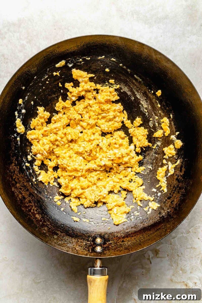 Scrambling eggs for fried rice in a wok. Eggs being scrambled in a hot wok with melted butter, showing the initial cooking stage.