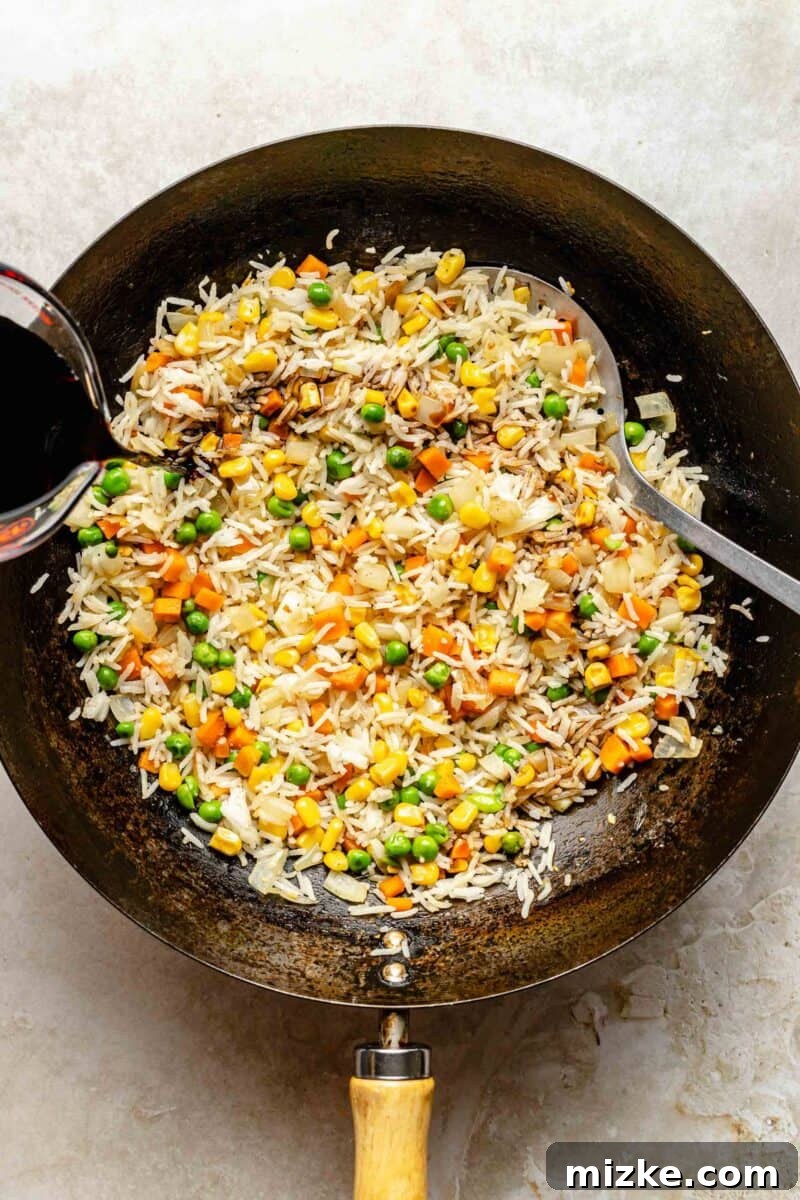 Adding soy sauce to fried rice in a wok for rich flavor. Soy sauce being poured evenly over rice and vegetables in a hot wok, ensuring even coating.