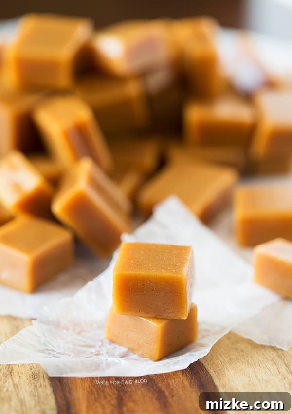 An array of freshly made apple cider caramels, some still in their wax paper wrappers, arranged on a baking sheet, highlighting their homemade charm and perfect square shape.