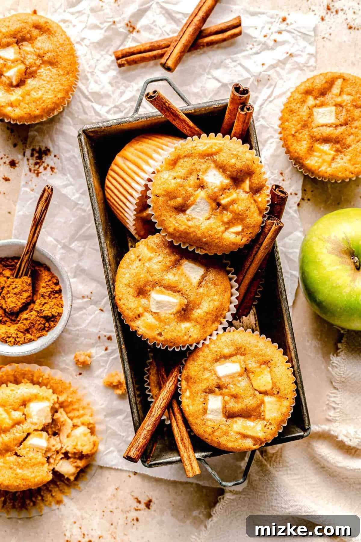 These moist, tender apple cinnamon muffins are filled with an abundance of apples and a heartwarming combination of honey and cinnamon. Apple cinnamon muffins in a loaf pan with cinnamon sticks.