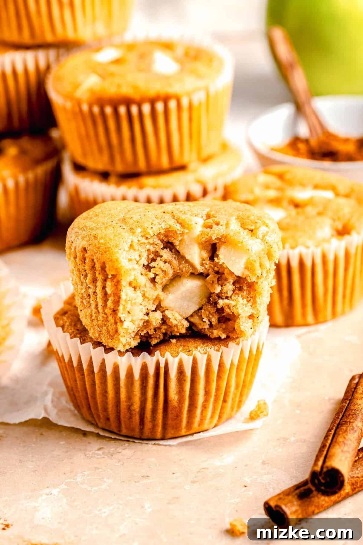 These moist, tender apple cinnamon muffins are filled with an abundance of apples and a heartwarming combination of honey and cinnamon. Apple cinnamon muffins stacked on top of each other. One of them has a bite taken out of it.