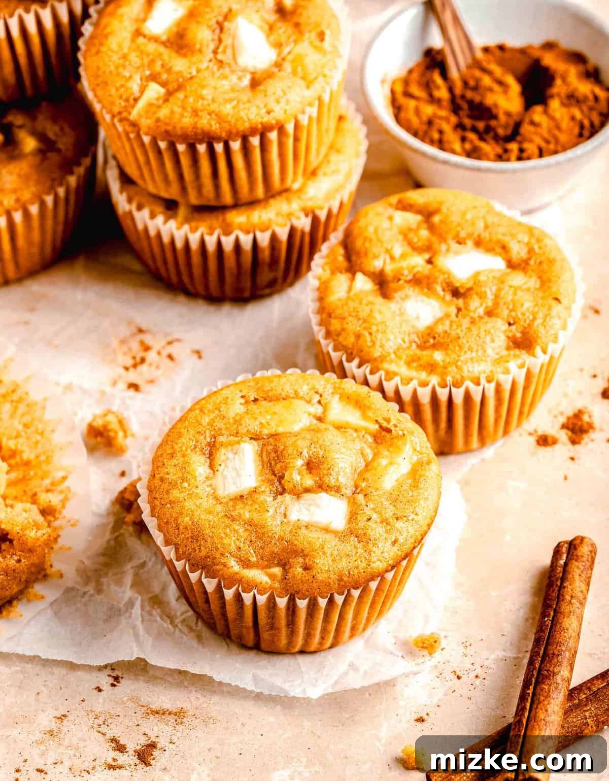 These moist, tender apple cinnamon muffins are filled with an abundance of apples and a heartwarming combination of honey and cinnamon. Apple cinnamon muffins near a bowl of cinnamon.