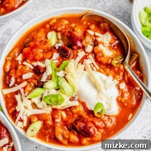 Close up of a bowl of turkey pumpkin chili, topped with cheese, green onions, and sour cream