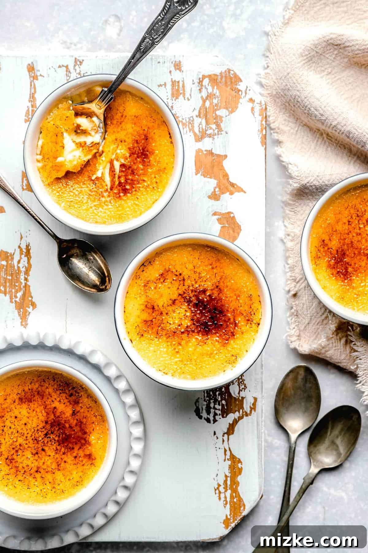Serve up individual portions of delectable homemade crème brûlée in charming ramekins. Overhead view of several ramekins of creamy crème brûlée, each with a spoon inserted, ready to be enjoyed.