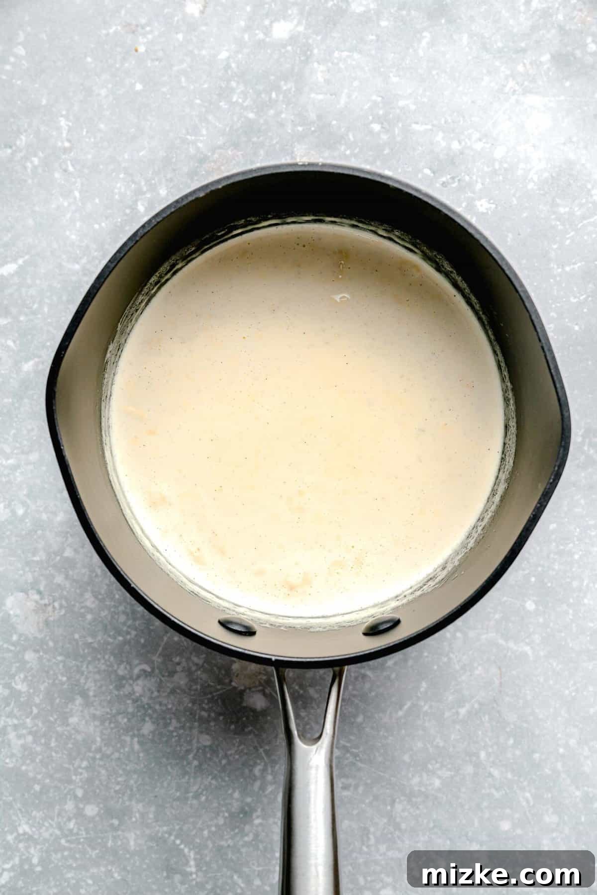 Infuse heavy cream with vanilla bean paste for rich flavor. Heavy cream infused with vanilla bean paste heating gently in a saucepan, small bubbles forming around the edges.