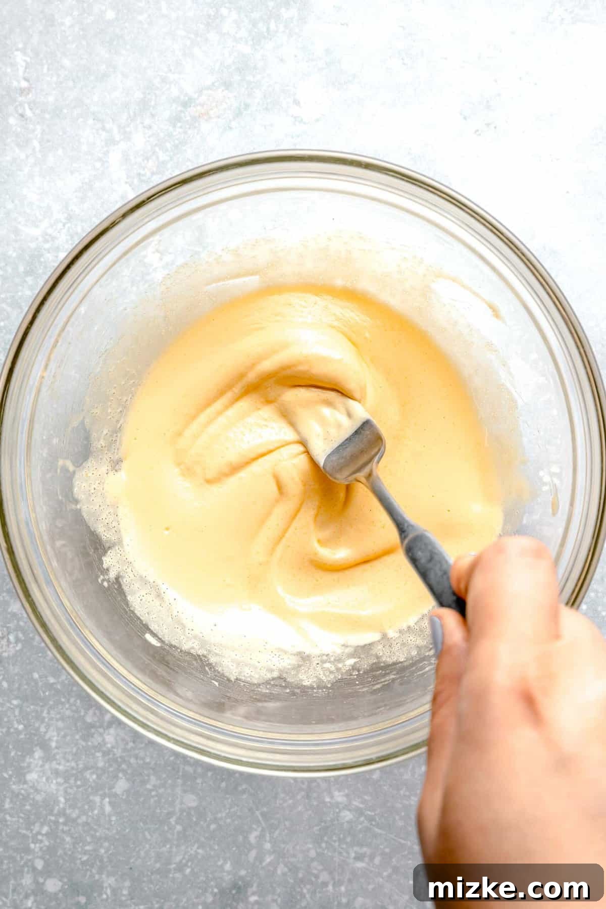 Whisk egg yolks, sugar, and salt until pale and creamy. A person whisking egg yolks, sugar, and salt together in a bowl to create the base for the custard.
