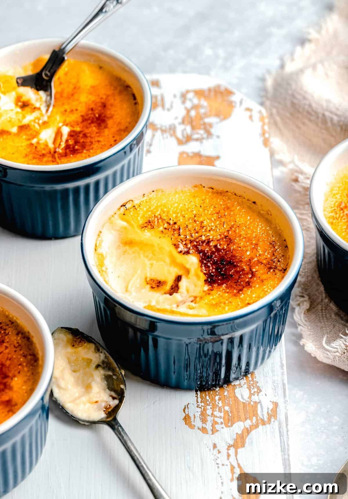 Enjoy the irresistible crack of the sugar crust on freshly torched crème brûlée. Several ramekins of crème brûlée, some with a spoonful removed, revealing the smooth custard, served with small spoons.