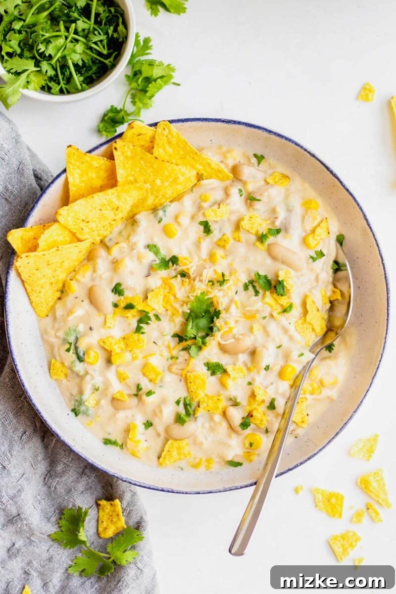White turkey chili in a large white speckled bowl with a blue rim. Cilantro and crushed tortilla chips garnish the top.