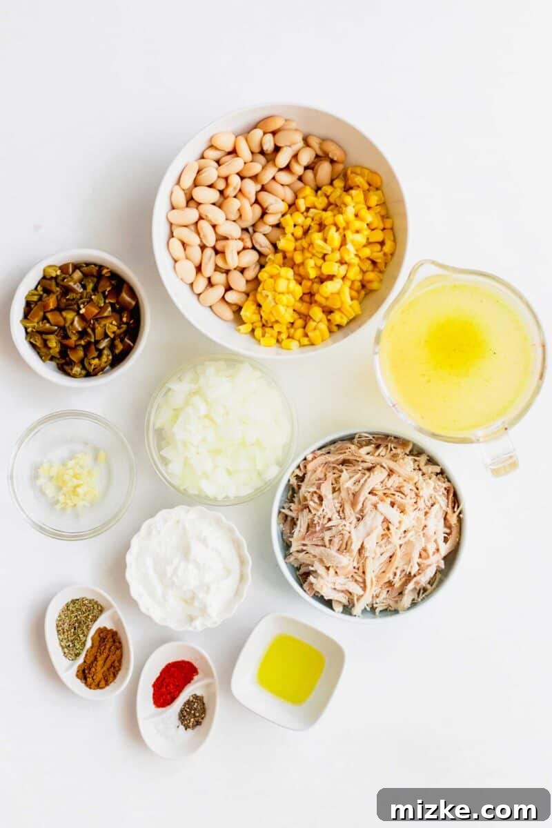 Overhead shot of all ingredients for white turkey chili: cannellini beans, corn, turkey stock, shredded turkey, olive oil, seasonings, cream cheese, diced onions, minced garlic, and chopped jalapenos.