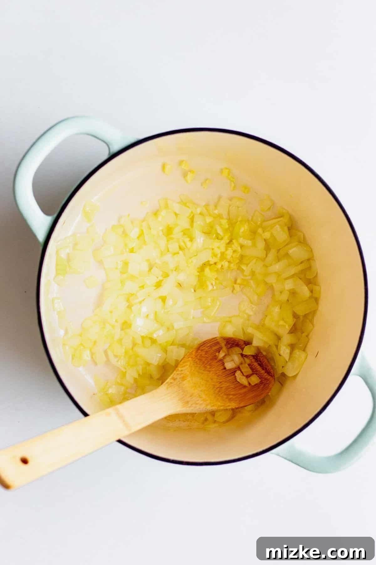 Sautéing onions and garlic in a large pot with a wooden spoon.