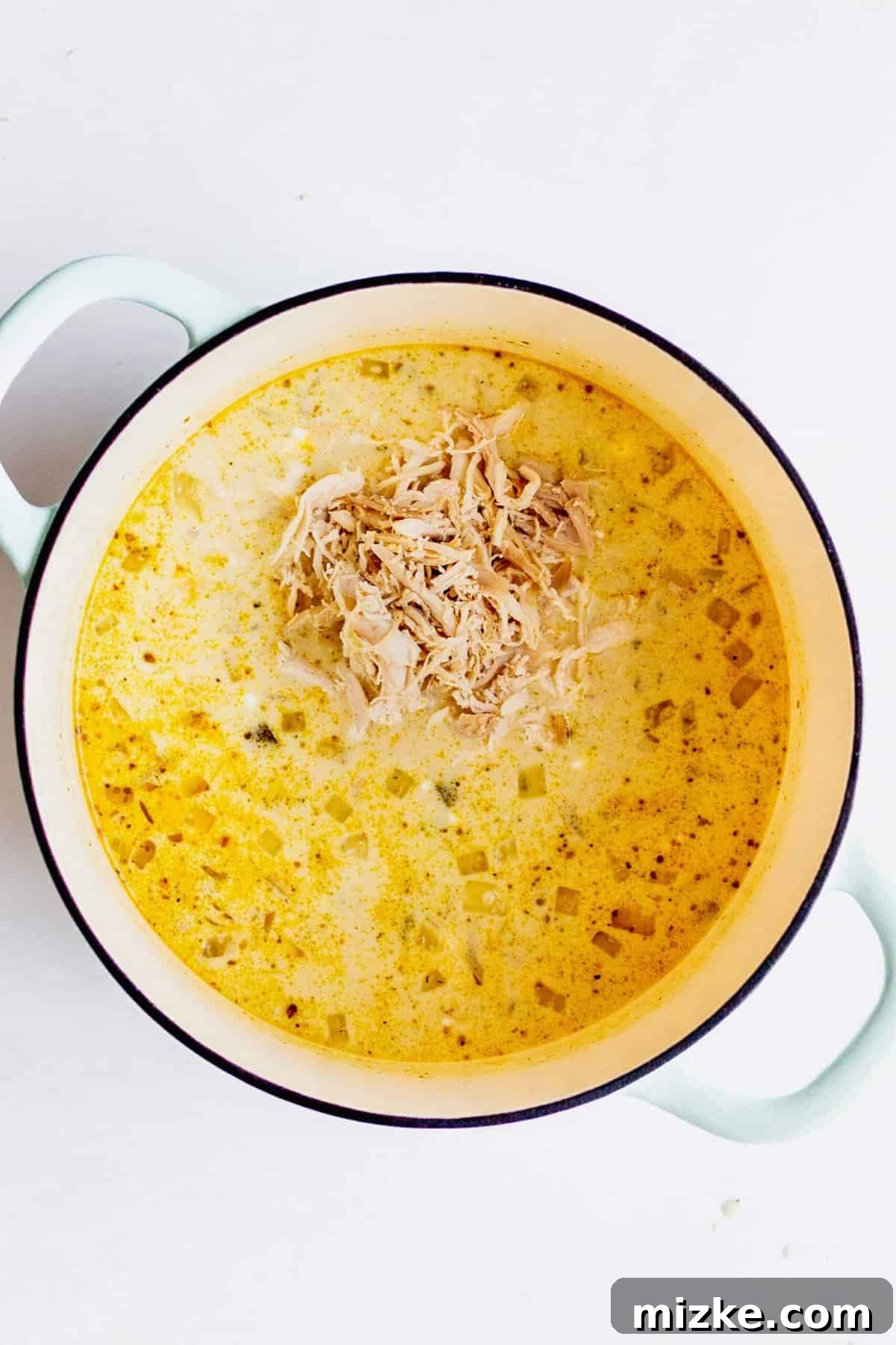 A large pile of shredded turkey is added into the soup in the large pot.