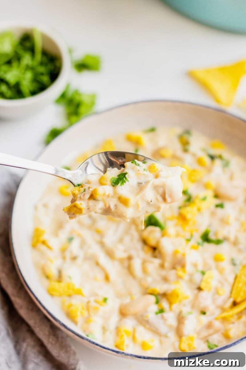 White turkey chili spooned out onto a spoon with the bowl in the background. Cilantro leaves and crushed tortillas are also seen in the background.
