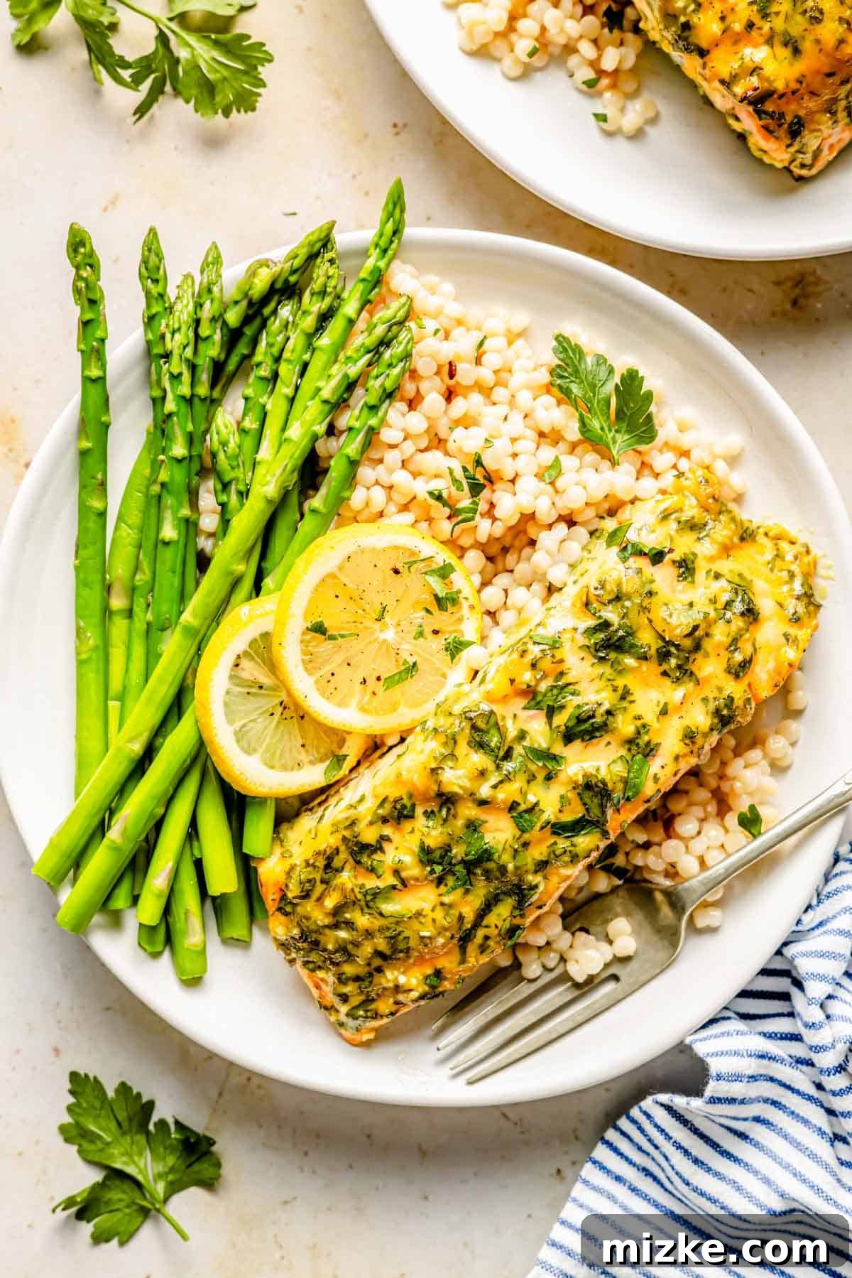 Sweet & Savory Dijon Salmon 4 a piece of honey dijon salmon on a white plate with pearl couscous, fresh asparagus, and lemon slices
