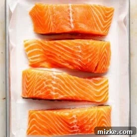 Sweet & Savory Dijon Salmon 6 four pieces of raw salmon on a parchment lined metal baking sheet