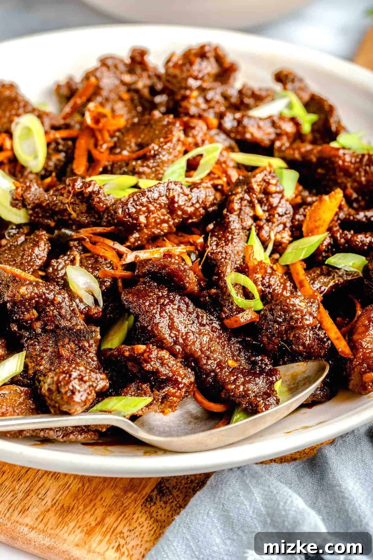 Homemade Crispy Beef: Fried strips of beef tossed in a sweet, savory, and spicy citrus sauce. A serving platter full of crispy beef, garnished with scallions.