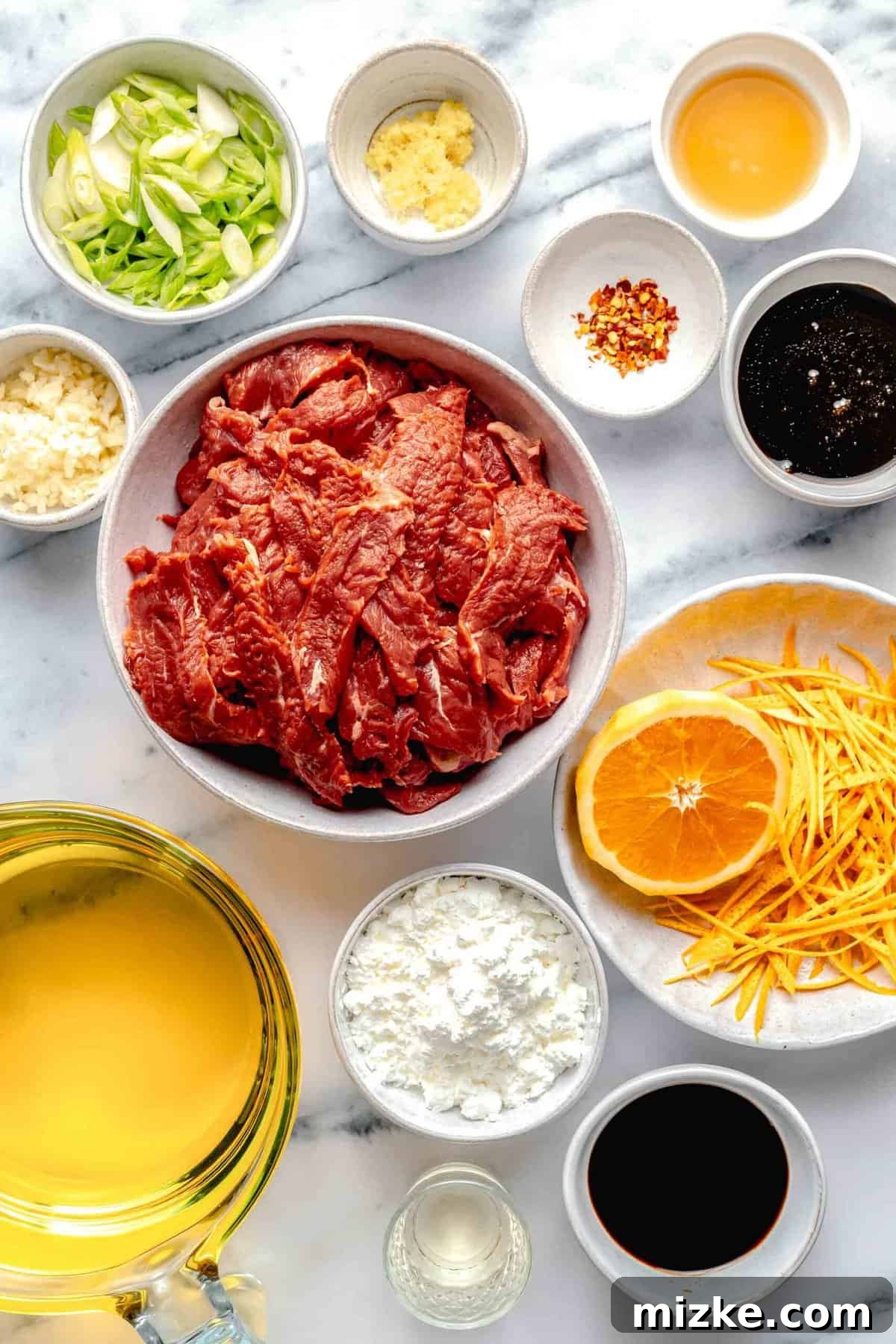 Key ingredients for a delectable homemade crispy beef with citrus sauce. Assorted fresh ingredients laid out for making crispy beef, including beef slices, orange, jalapeño, and sauces.